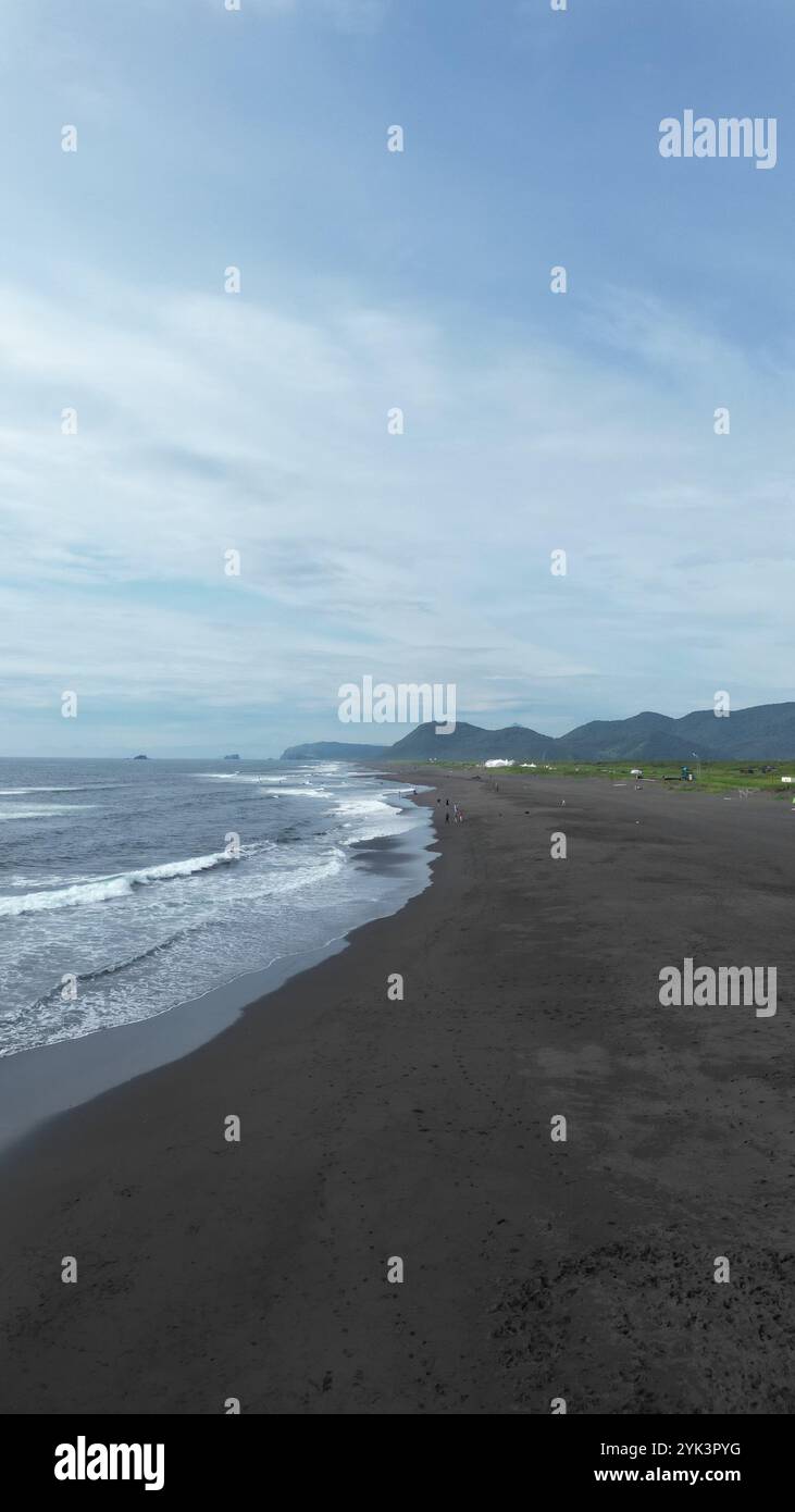 Blick aus der Vogelperspektive auf den Strand von Khalaktyrsky. Eine ruhige Küstenlandschaft mit einem atemberaubenden schwarzen Sandstrand und majestätischen Bergen Stockfoto