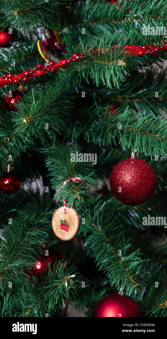 Festlich geschmückter Weihnachtsbaum mit roten Ornamenten und handgefertigtem Holzschmuck, der den Weihnachtsgeist und die saisonale Wärme einfängt. Stockfoto