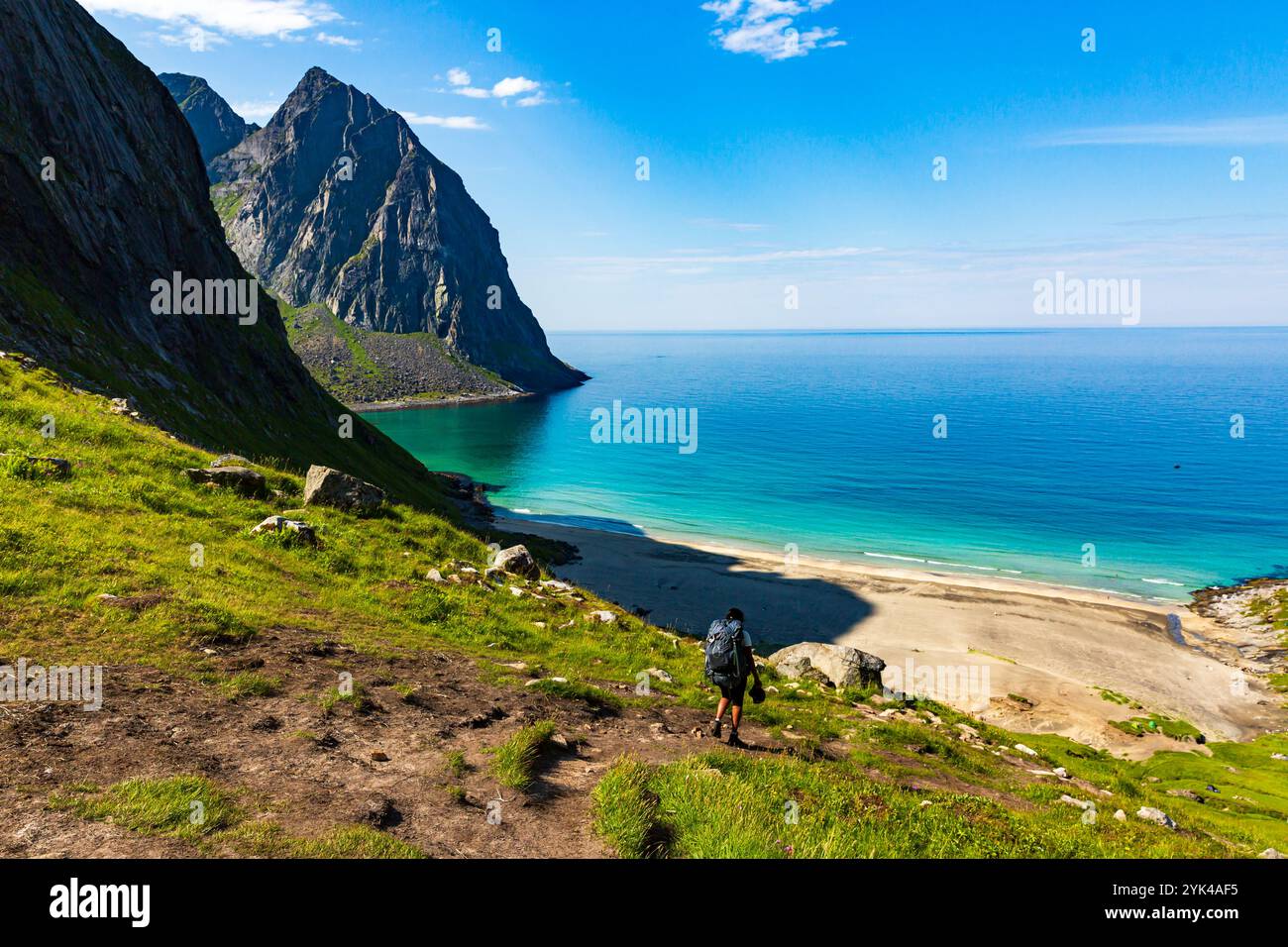 Ein Wanderer auf dem Weg zum Kvalvika Beach in Lofoten, Norwegen, umgeben von zerklüfteten Klippen und atemberaubendem Blick auf die Küste an einem perfekten Sommertag Stockfoto