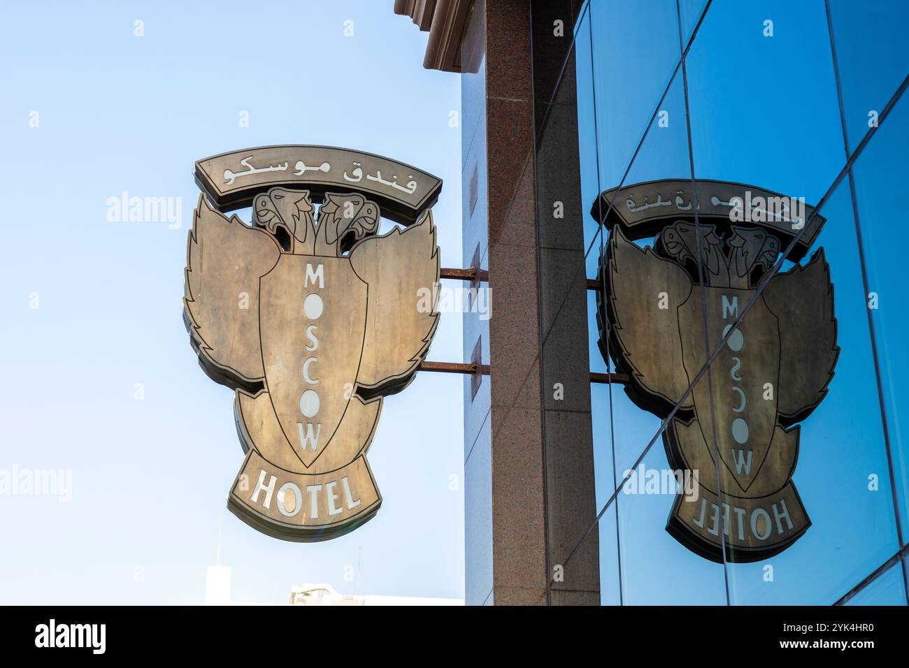 Eine Nahaufnahme des hängenden doppelköpfigen Adleremblems für das Moscow Hotel spiegelt sich in der blauen Glasfassade des Gebäudes in Dubai, VAE. Stockfoto