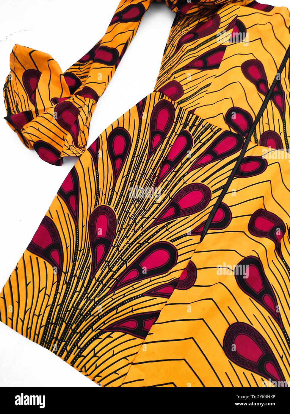 Afrikanisch gemusterte Runya-Kleid mit Details für Anlässe, gelbe Baumwolle mit langen geschwollenen Ärmeln und rotem Paisley-Druck auf weißem Hintergrund, Kleidung Stockfoto