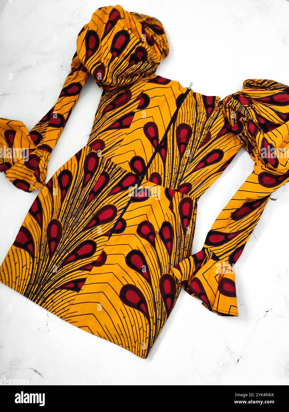 Afrikanisch gemusterte Runya-Kleid mit Details für Anlässe, gelbe Baumwolle mit langen geschwollenen Ärmeln und rotem Paisley-Druck auf weißem Hintergrund, Kleidung Stockfoto