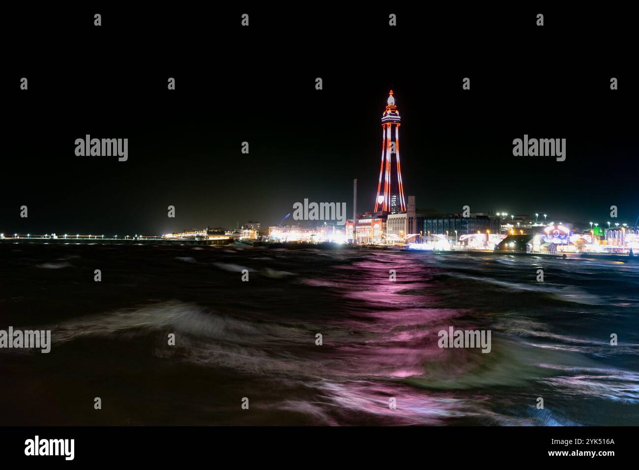 Der Blackpool Tower, der für die Beleuchtung von 2024 beleuchtet ist, strahlt ein farbenfrohes Leuchten über das Wasser der Irischen See Stockfoto