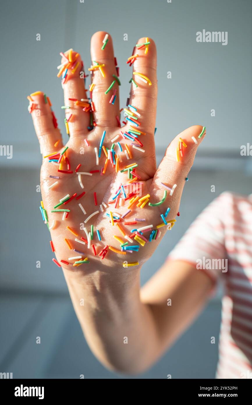 Frauenhand bedeckt mit bunten Zuckerstreuseln für Bäckerei und farbige Backdekorationen. Stockfoto