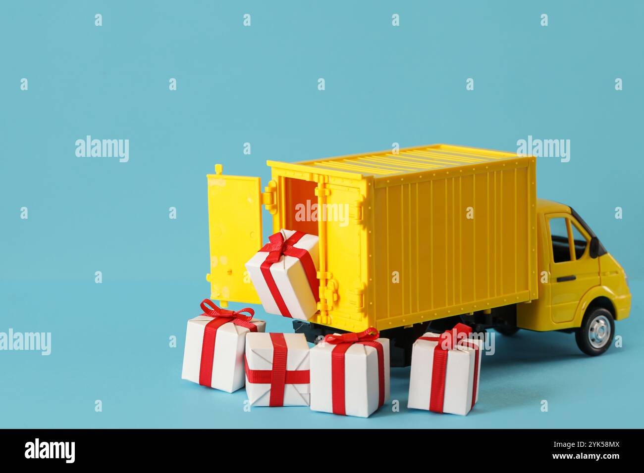 Gelbe Geschenkbox für Lkw-Lieferung auf blauem Hintergrund. Frachttransport, Lieferservice. Transportunternehmen. Infrastruktur und Logistik. Entladen Stockfoto