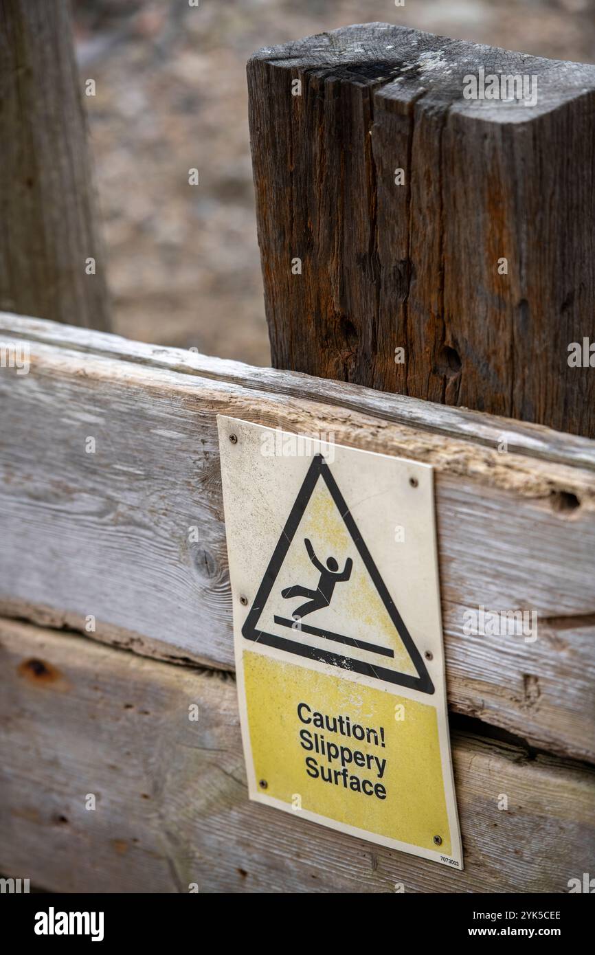 Achtung: Warnschild auf rutschigem Untergrund, alter Holzsteg mit Rutschgefahr gelbes Warnschild Stockfoto