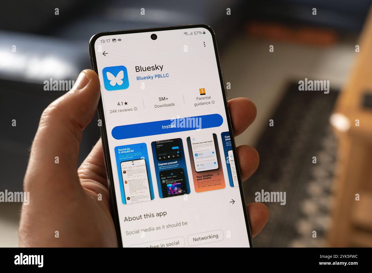 Man hält ein Smartphone mit dem Installationsbildschirm für Bluesky, einen öffentlichen Microblogging-Dienst in sozialen Medien, der Follower von X anzieht Stockfoto