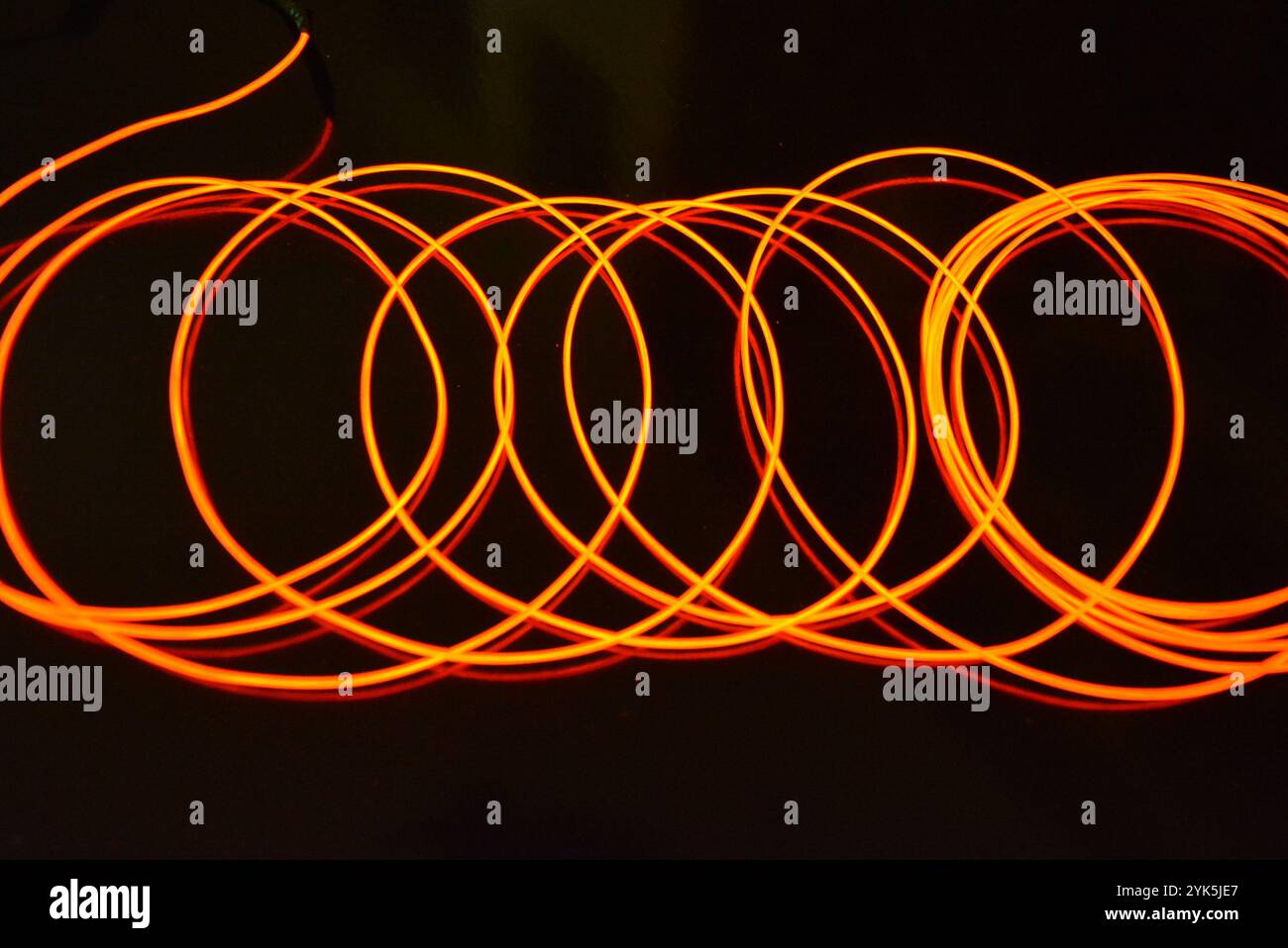 Ungewöhnliches, dünnes rotes Gewinde, verdrillter Draht, strukturelles und gebogenes Kabel. Neon-Elektrolumineszenzkabel, Draht, Kunststoff strahlt Neonlicht gleichmäßig aus. Stockfoto