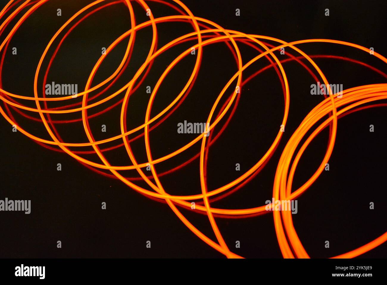 Ungewöhnliches, dünnes rotes Gewinde, verdrillter Draht, strukturelles und gebogenes Kabel. Neon-Elektrolumineszenzkabel, Draht, Kunststoff strahlt Neonlicht gleichmäßig aus. Stockfoto