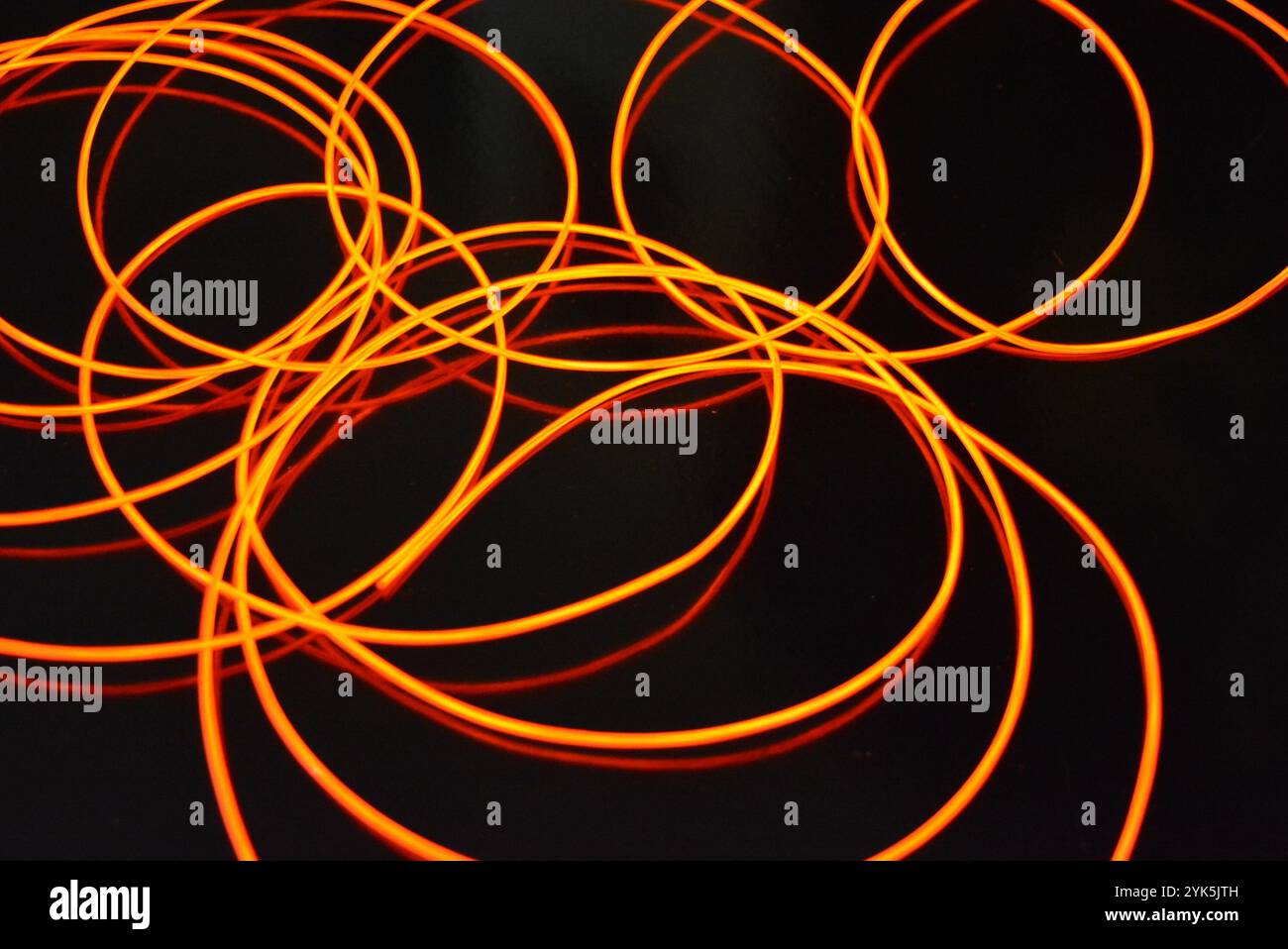 Ungewöhnliches, dünnes rotes Gewinde, verdrillter Draht, strukturelles und gebogenes Kabel. Neon-Elektrolumineszenzkabel, Draht, Kunststoff strahlt Neonlicht gleichmäßig aus. Stockfoto