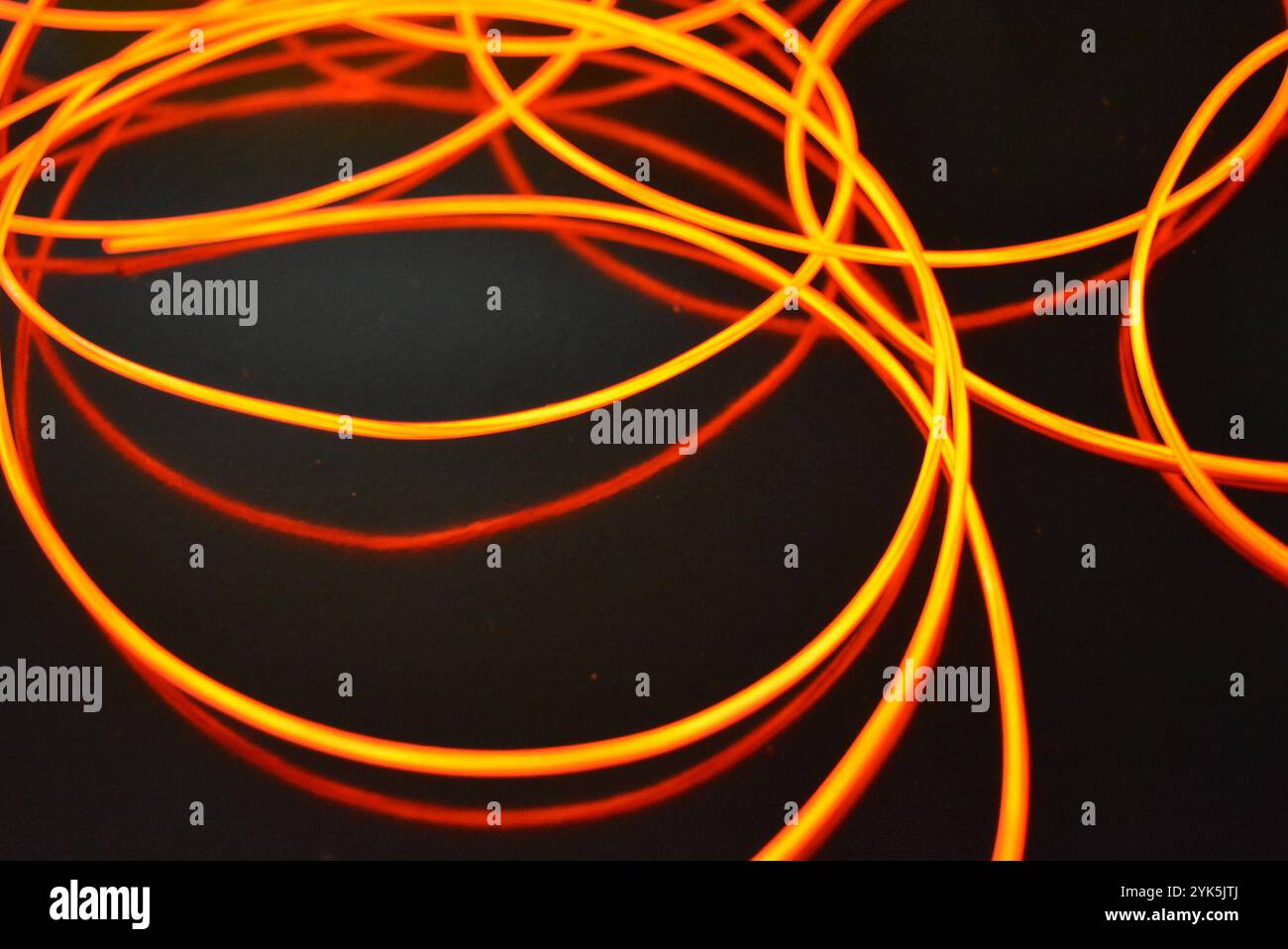 Ungewöhnliches, dünnes rotes Gewinde, verdrillter Draht, strukturelles und gebogenes Kabel. Neon-Elektrolumineszenzkabel, Draht, Kunststoff strahlt Neonlicht gleichmäßig aus. Stockfoto