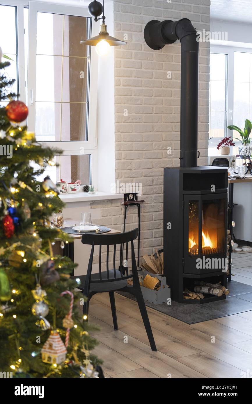 Das festliche Innere des Hauses ist für Weihnachten und Neujahr im Loftstil dekoriert mit schwarzem Herd, Kamin, Weihnachtsbaum. Warmes Studio-Zimmer mit Whi Stockfoto