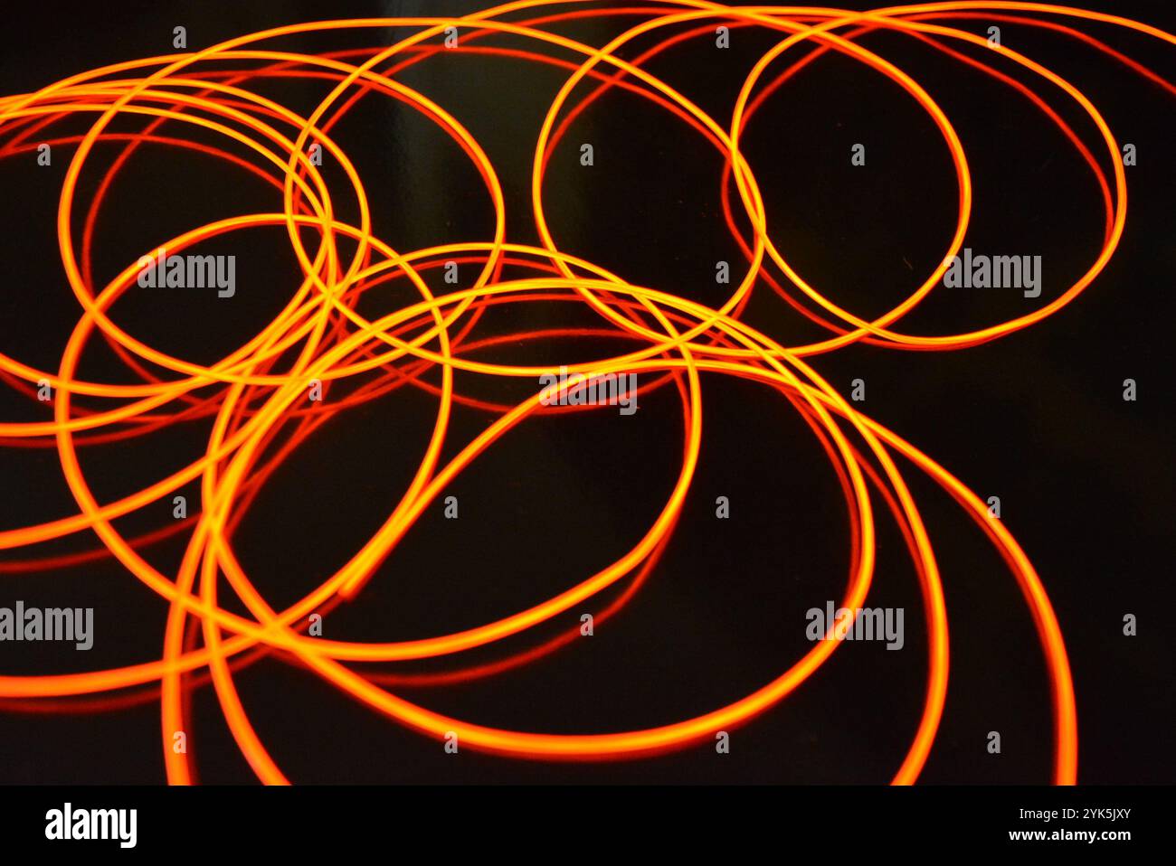 Ungewöhnliches, dünnes rotes Gewinde, verdrillter Draht, strukturelles und gebogenes Kabel. Neon-Elektrolumineszenzkabel, Draht, Kunststoff strahlt Neonlicht gleichmäßig aus. Stockfoto