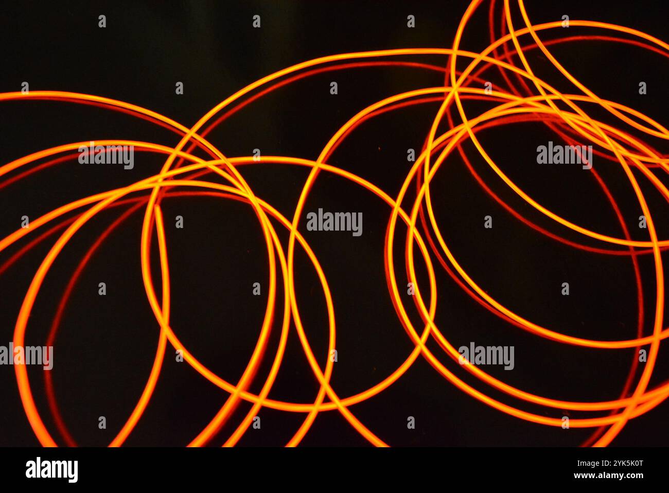 Ungewöhnliches, dünnes rotes Gewinde, verdrillter Draht, strukturelles und gebogenes Kabel. Neon-Elektrolumineszenzkabel, Draht, Kunststoff strahlt Neonlicht gleichmäßig aus. Stockfoto