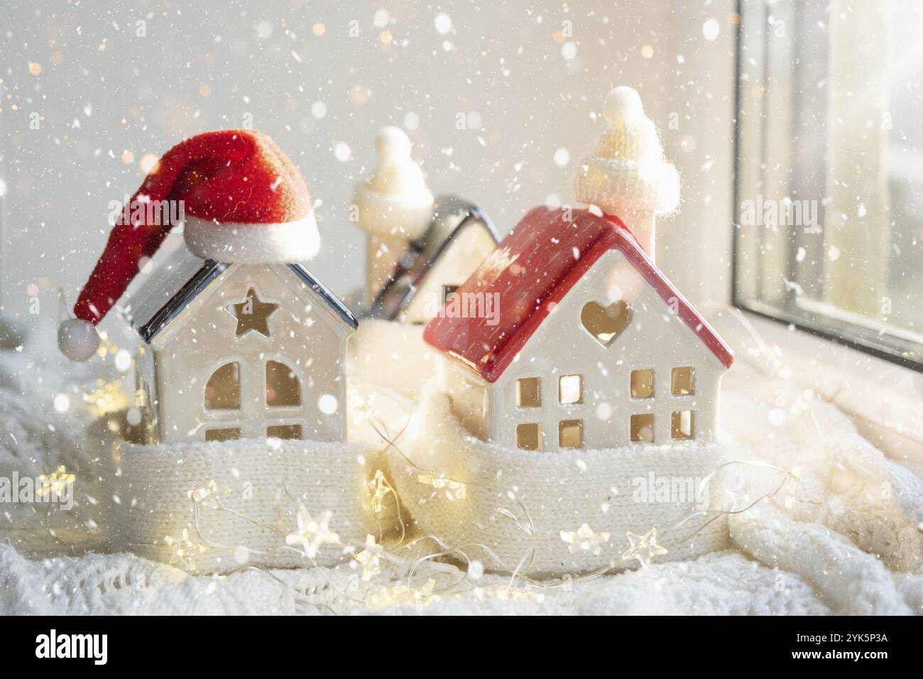 Gemütliches Haus ist mit einem Hut und Schal in einem Schneesturm gewickelt - Fensterbank Dekor. Winter, Schnee, Hausisolierung, Schutz vor Kälte und schlechtem Wetter, Zimmer Stockfoto