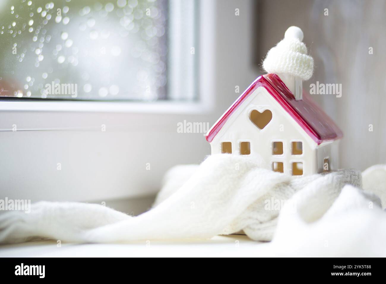 Gemütliches Haus ist mit einem Hut und Schal in einem Schneesturm gewickelt - Fensterbank Dekor. Winter, Schnee, Hausisolierung, Schutz vor Kälte und schlechtem Wetter, Zimmer Stockfoto