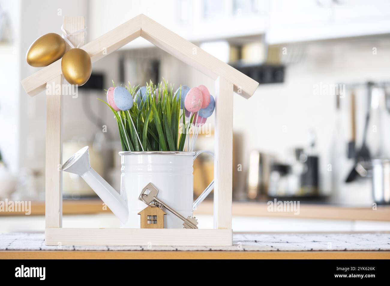 Schlüssel und winziges Haus mit gemütlichem Haus mit Osterdekor mit farbigen Eiern auf dem Tisch der Küche. Bauen, Design, Projekt, Umzug in ein neues Haus, Hypothek, Insur Stockfoto