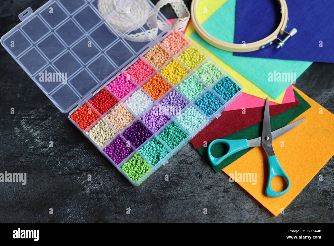 DIY-Projekt im Machen. Foto von oben mit bunten Glasperlen, Filzstoff und Schere auf dunkelgrauem Schreibtisch. Handarbeit in Bearbeitung. Stockfoto