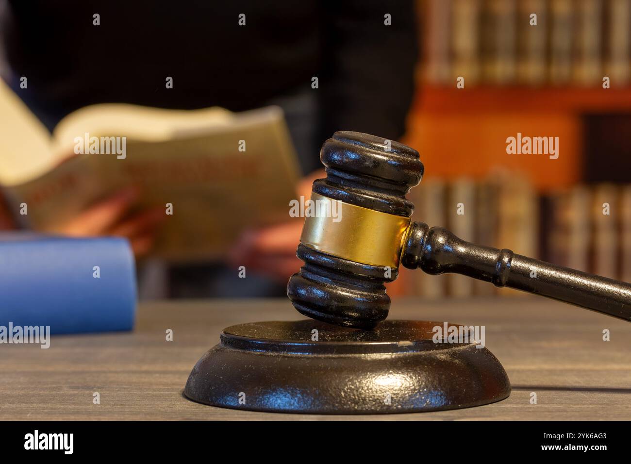 Nahaufnahme eines Jury-Gavels, im Hintergrund liest ein Mann ein Gesetzbuch (Symbolbild) Stockfoto