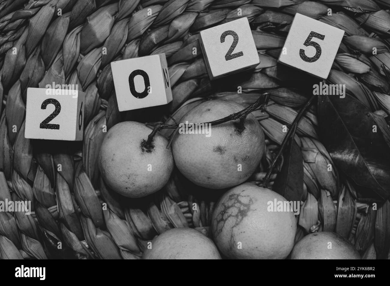 Mandarinen und Holzwürfel mit dem Jahr 2025 liegen auf einem Strohkorb, Schwarz-weiß-Foto Stockfoto
