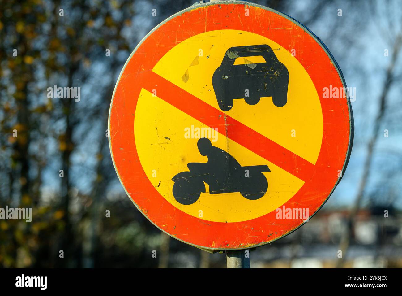 Ein kreisförmiges Schild weist darauf hin, dass Autos und Motorräder in diesem Gebiet verboten sind. Die hellen Farben heben sich von einem klaren Himmel und den Bäumen in der Nähe ab Stockfoto