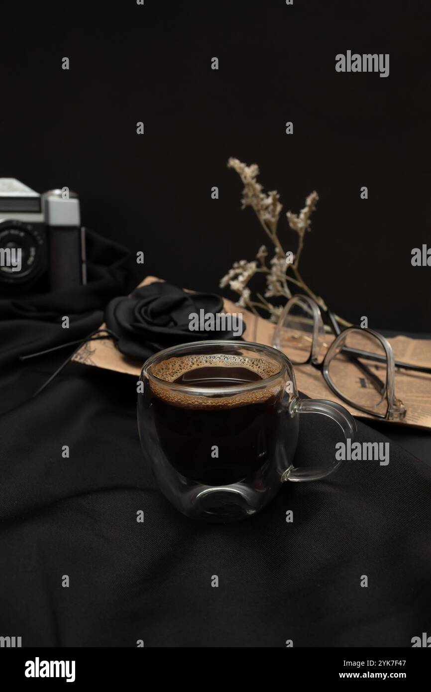 Schwarzer Kaffee in einer beleuchteten Tasse mit zusätzlichen Elementen und schwarzem Hintergrund. Stockfoto