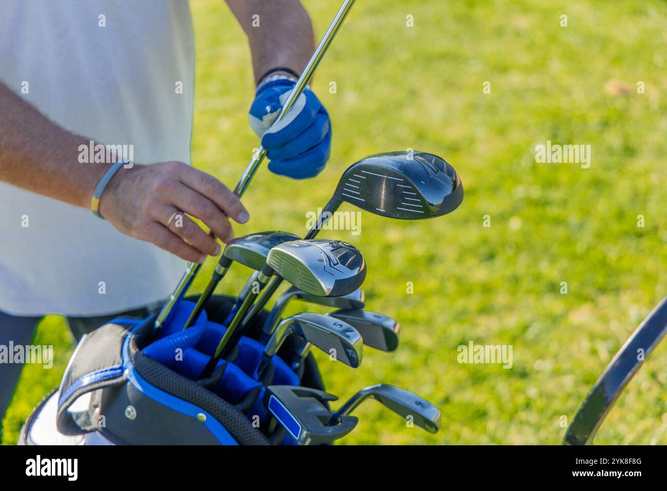 Nahaufnahme der Hände eines älteren Golfspielers, während er sorgfältig einen Schläger aus seiner Golftasche auswählt, wobei die Ausrüstung und die Liebe zum Detail bei der Vorbereitung hervorgehoben werden Stockfoto