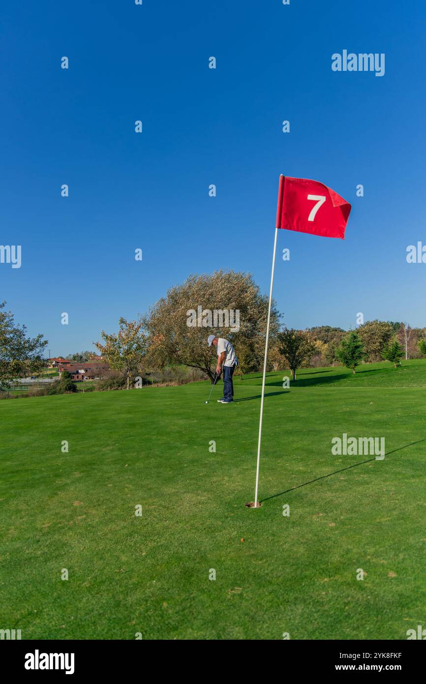 Vertikaler Golfer, der einen Putt anlegt und den Ball vorsichtig in Richtung der Flagge auf dem Grün richtet. Das Bild zeigt die Konzentration des Golfers und die Stockfoto