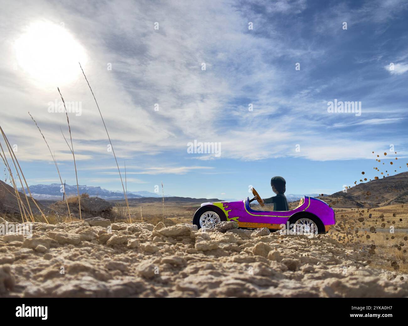Rennwagen und Fahrer sehen ferne Berge in der hohen Wüste. Der violette Rennfahrer durchquert Schlamm und Felsen, die im Hintergrund in der Nähe der Straße auftauchen. Stockfoto