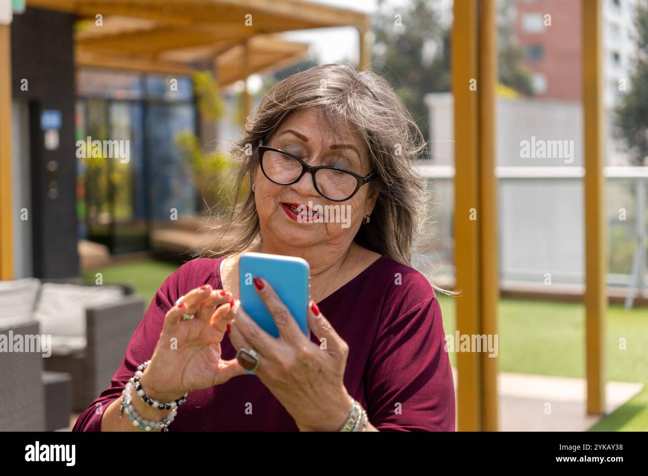 Porträt einer älteren Frau mit Brille, die morgens draußen ihr Handy benutzt Stockfoto
