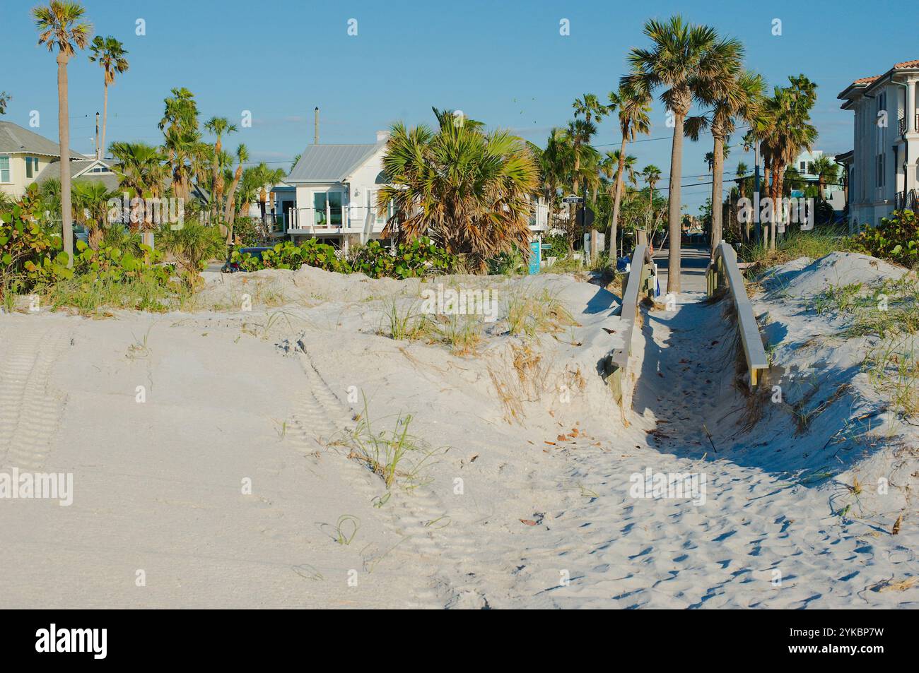 Horizontaler Blick vom Pass-a-Grille Beach Florida in Richtung Ufer. Fußspuren, Holzbrücke zum Strand, Hafer, grüne Palmen und blauer Himmel Stockfoto
