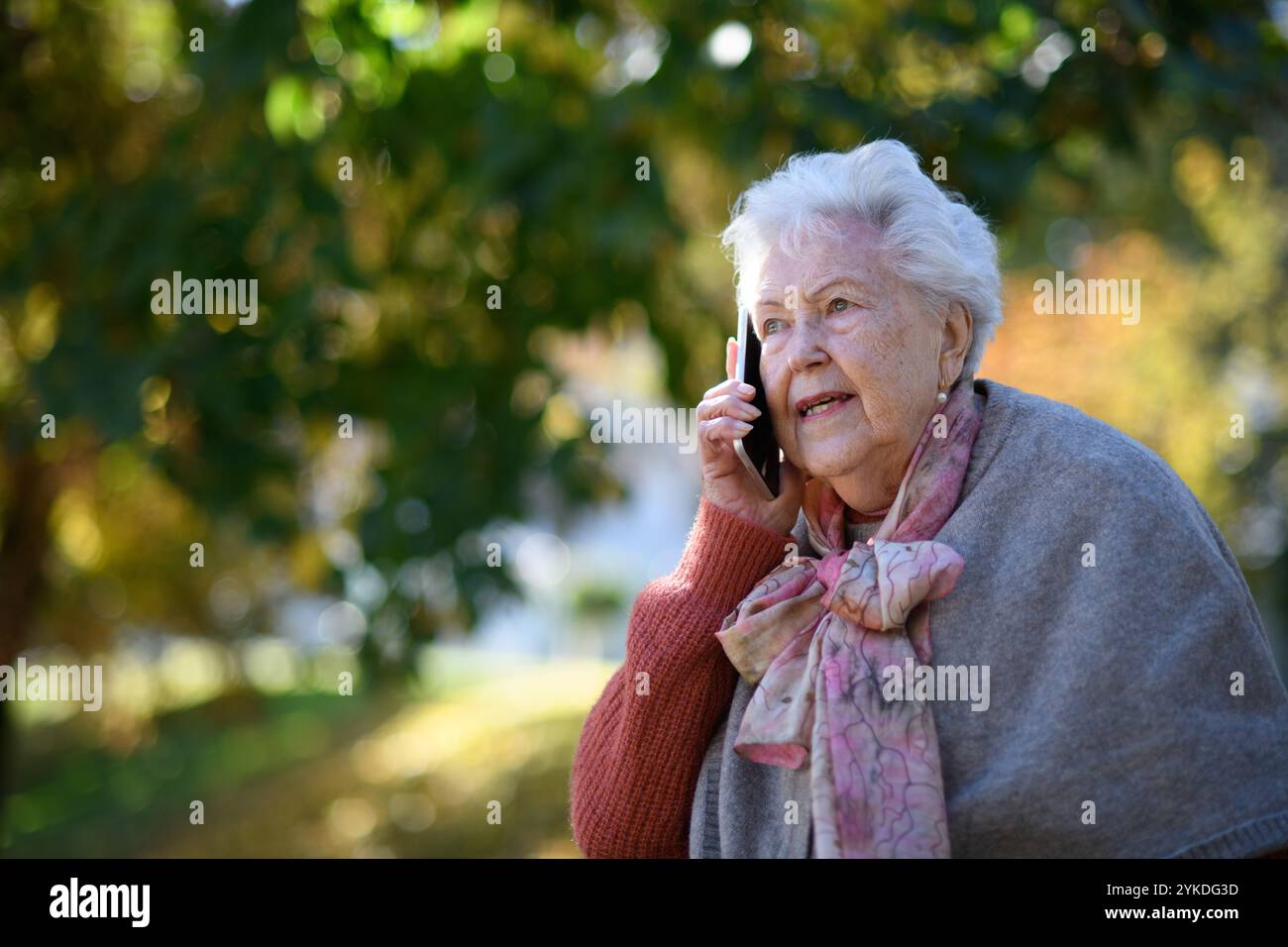 Eine ältere Frau im Park, die ein Smartphone hält und mit jemandem telefoniert. Stockfoto