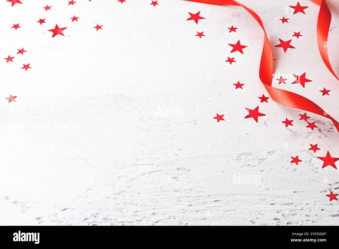 Hellblauer Hintergrund mit roten Satinbändern und Konfetti-Sternen, Kopierraum, minimalistischer Stil, festlicher Hintergrund für Design Stockfoto