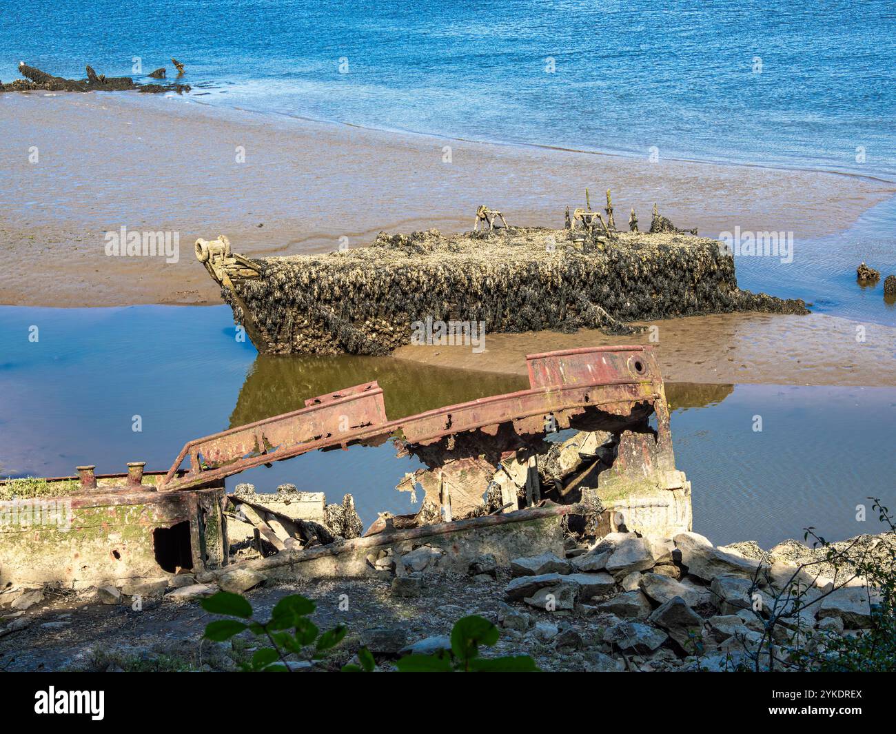 Ein verrostetes Schiffswrack, das teilweise in Sand und Wasser an einem Strand von Lanester-Kerhervy in der Bretagne untergetaucht ist Stockfoto