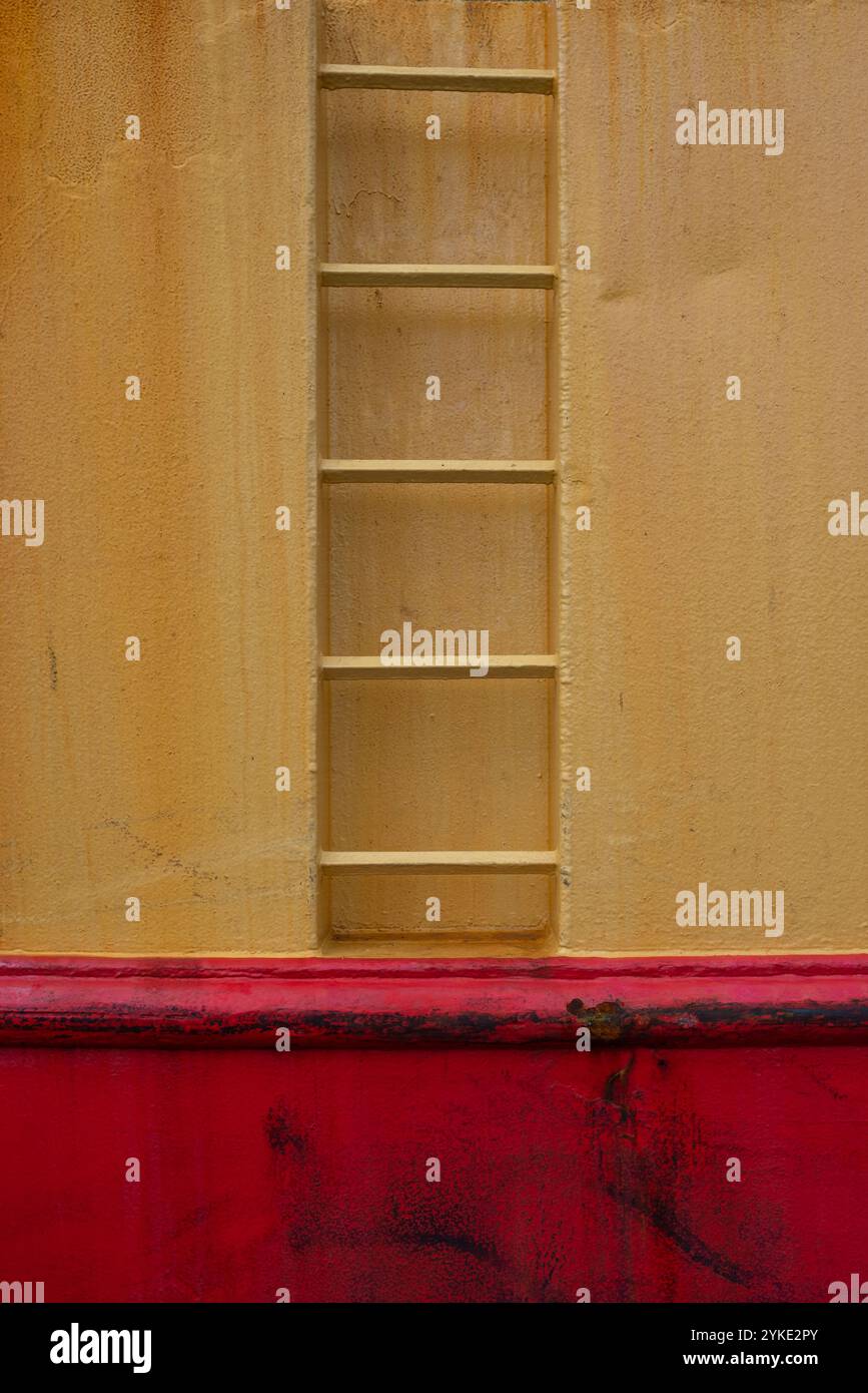 Kontrastierende Farben in Gelb und Rot mit einer Leiter an der Seite eines Schiffes. Stockfoto