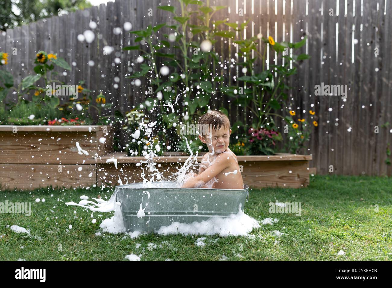 Kinder spritzen im Freien in einer Metallwanne, umgeben von Gartenblumen. Stockfoto