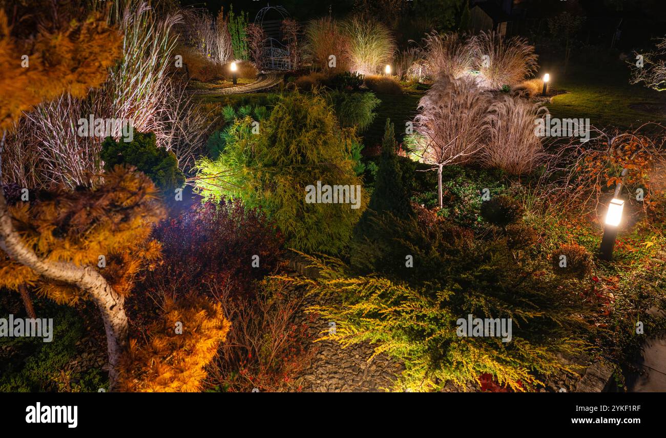 Ein ruhiger Garten erwacht nachts mit warmen Lichtern, farbenfrohen Herbstpflanzen und üppigem Grün in einer ruhigen Umgebung zum Leben. Stockfoto