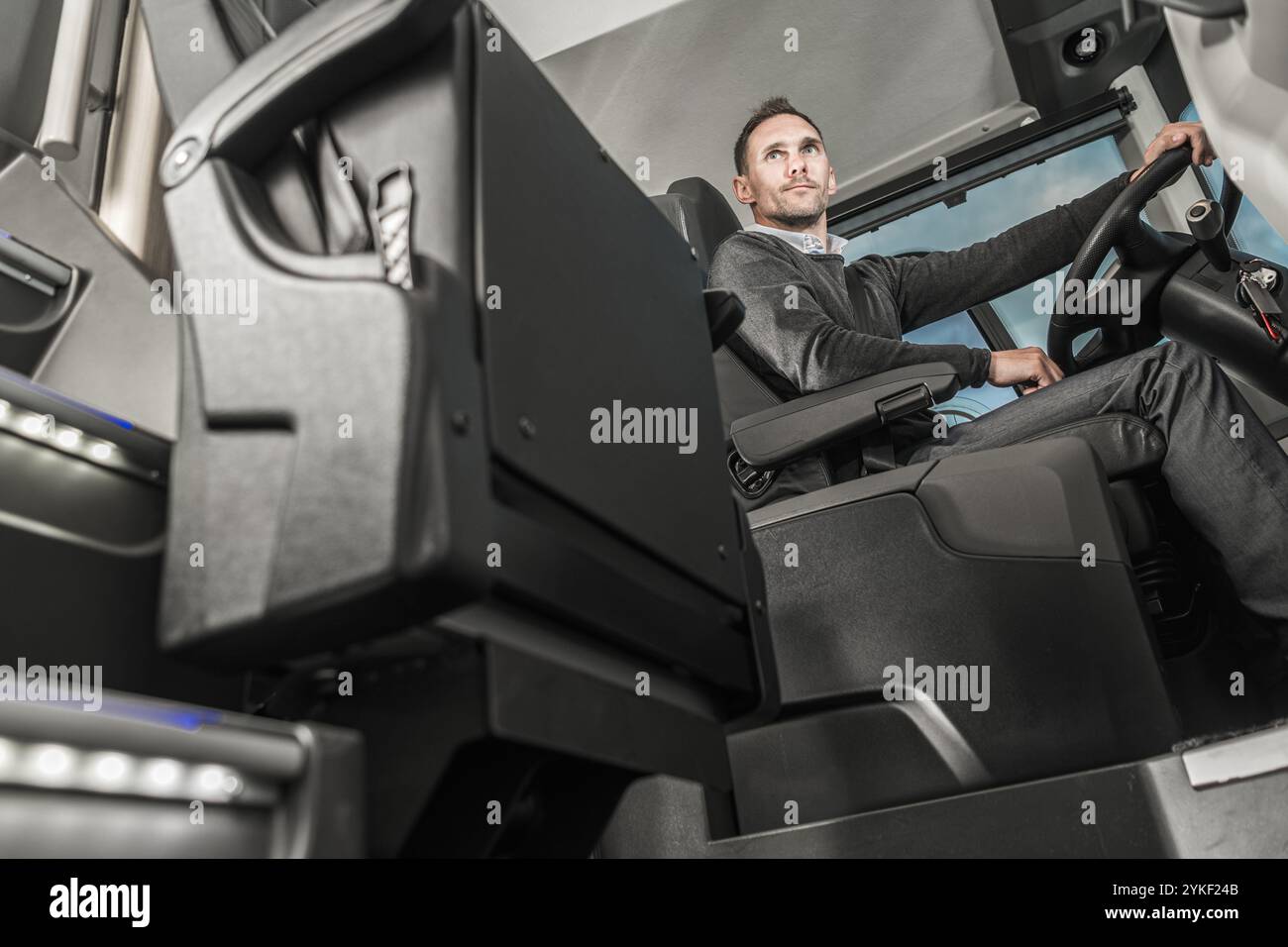Ein erfahrener Busfahrer konzentriert sich auf die Navigation eines modernen Busses durch die belebten Straßen der Stadt am helllichten Tag und zeigt fachkundige Kontrolle und PR Stockfoto
