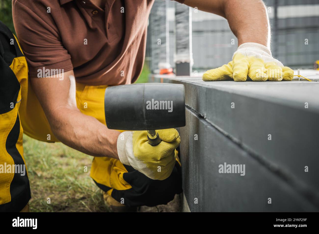 Ein Bauarbeiter, der Handschuhe trägt, legt tagsüber mit einem Gummihammer in einer belebten Stadtumgebung sorgfältig Pflastersteine auf. Stockfoto