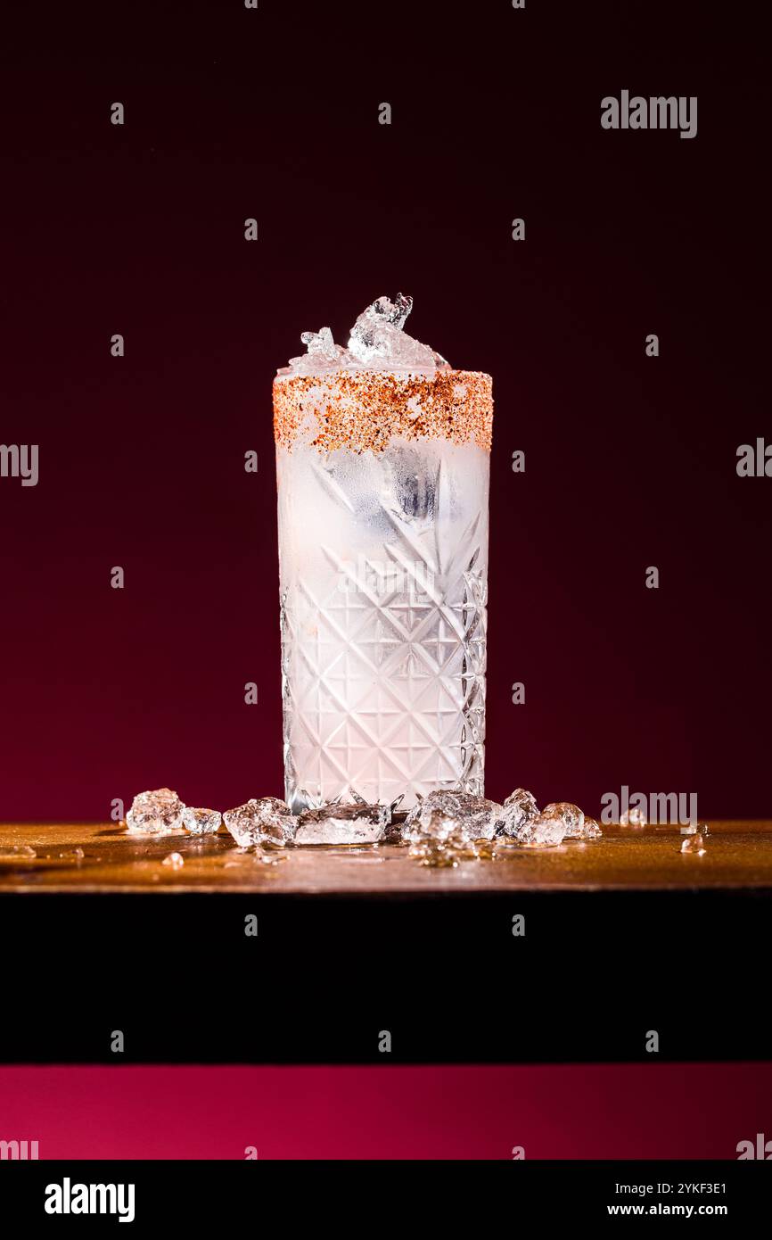 Ein Paloma-Cocktail in einem gemusterten Glas, verziert mit einem gesalzenen Rand und gefüllt mit erfrischendem Eis. Das Getränk steht vor einer stimmungsvollen, dunklen Kulisse Stockfoto