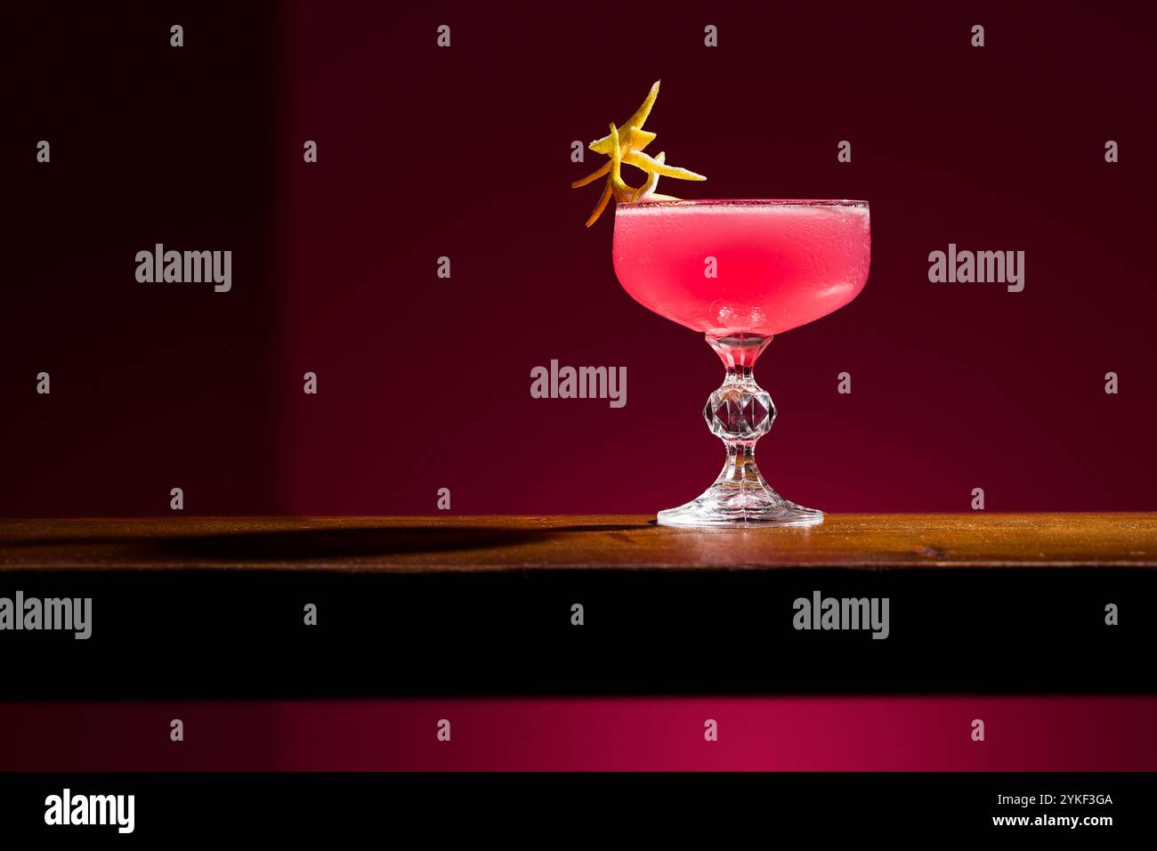 Cosmopolitan Cocktail wird elegant auf einer Holzoberfläche vor dunklem Hintergrund präsentiert. Das pulsierende pinkfarbene Getränk wird mit einem Zitrusduft, Crea, garniert Stockfoto