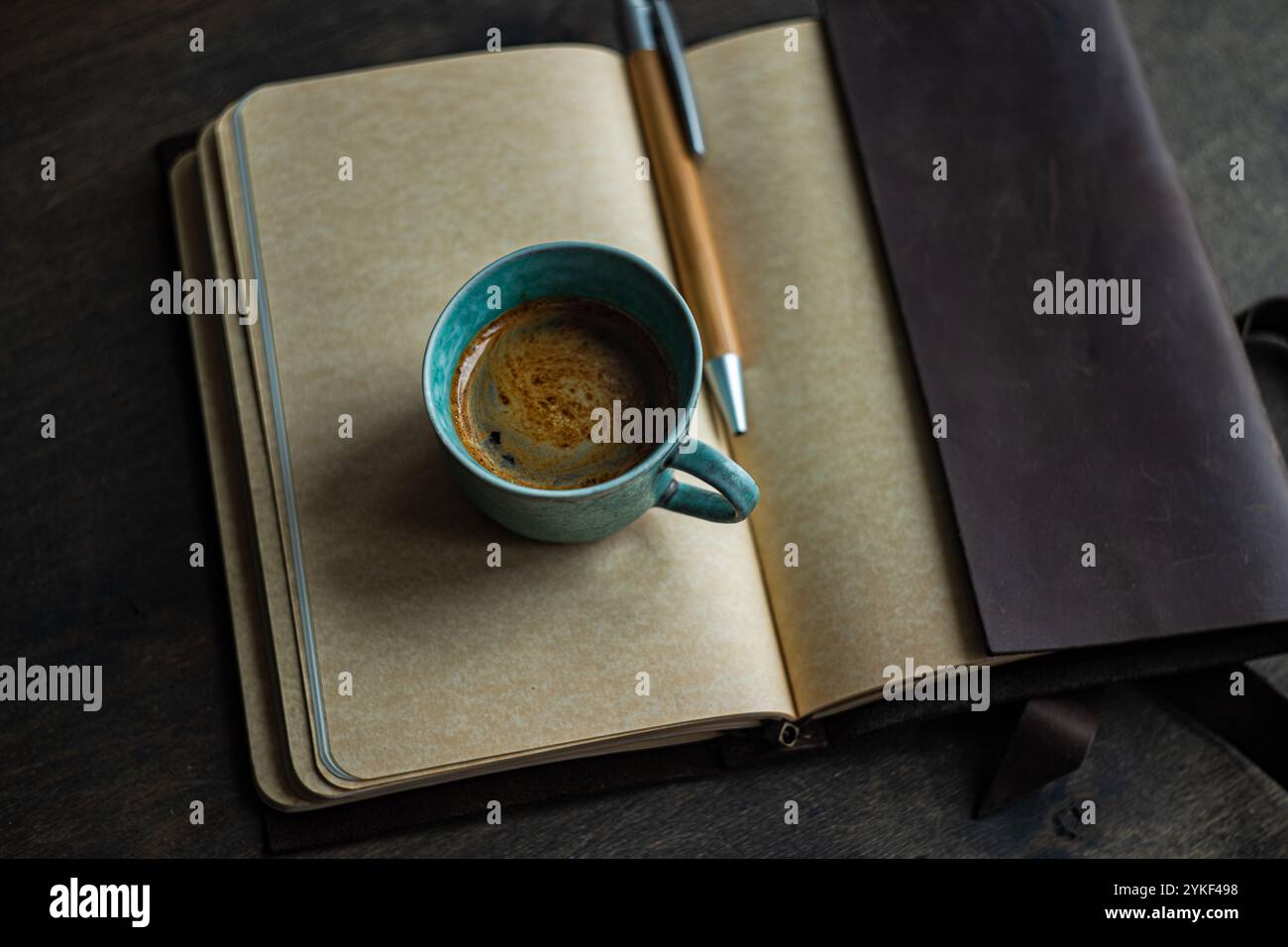Draufsicht einer Kaffeetasse auf einem offenen Notizblock neben einem Stift und einer Lederhülle, die einen organisierten Arbeitsbereich darstellt. Stockfoto