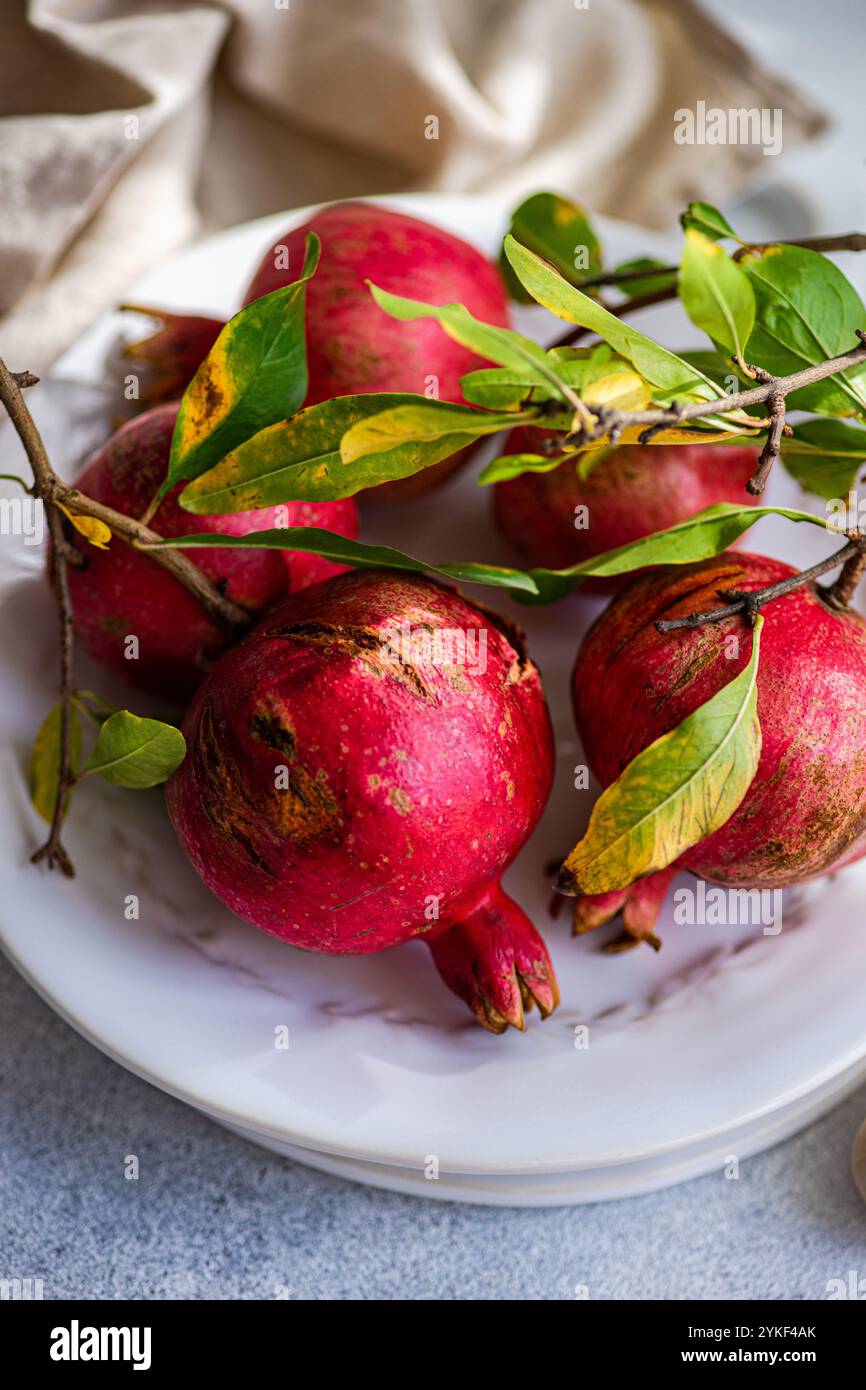 Nahaufnahme reifer roter Granatäpfel mit leuchtend grünen Blättern auf einer weißen Keramikplatte, die den Farbkontrast und die frische Fruchtstruktur betont. Stockfoto