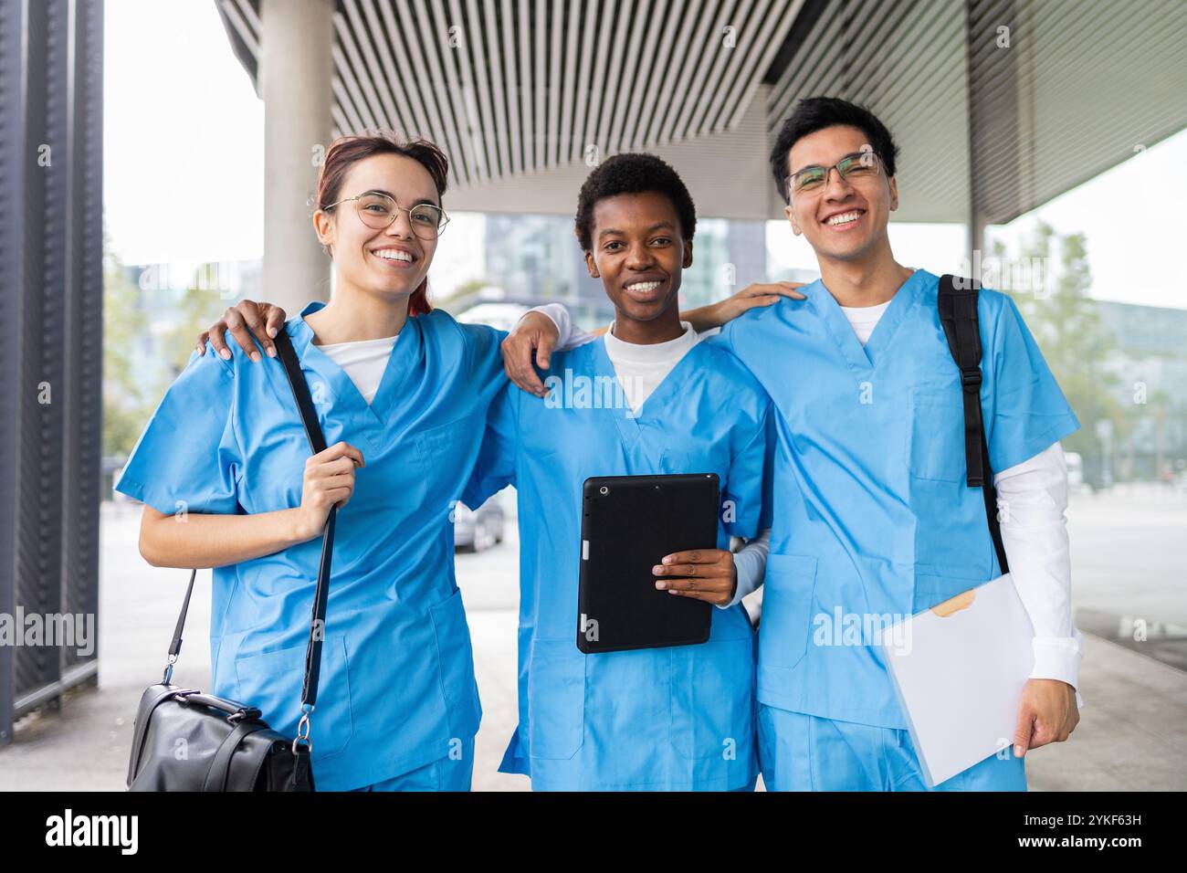 Drei glückliche Krankenpflegeschülerinnen und -Studenten stehen zusammen vor ihrer Universität und teilen einen freudigen Moment Stockfoto