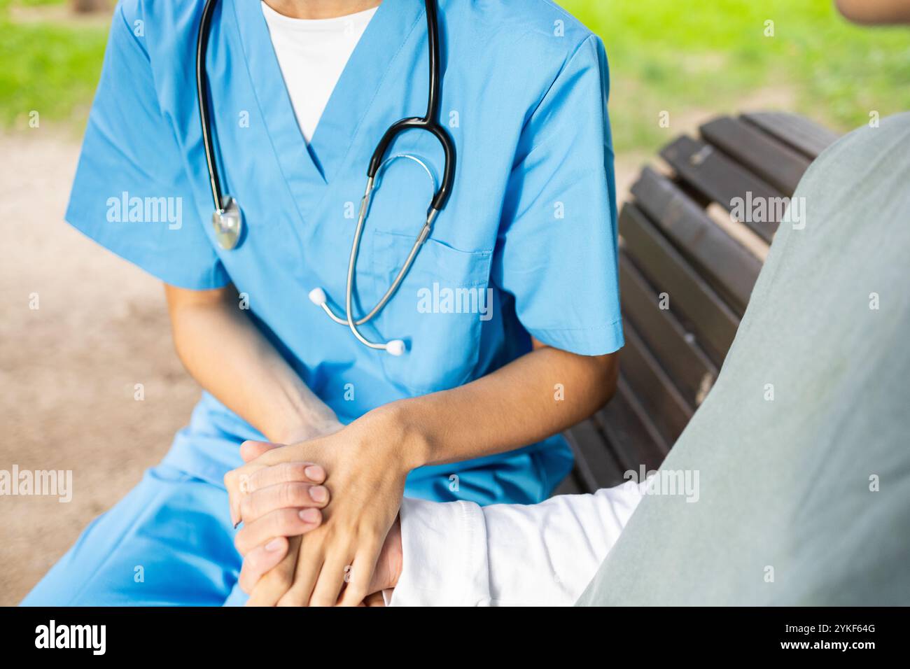 Eine Krankenschwester in blauen Peelings bietet dem Patienten Komfort und hält einen Moment der Pflege und des Einfühlens in einer ruhigen Umgebung im Freien fest Stockfoto