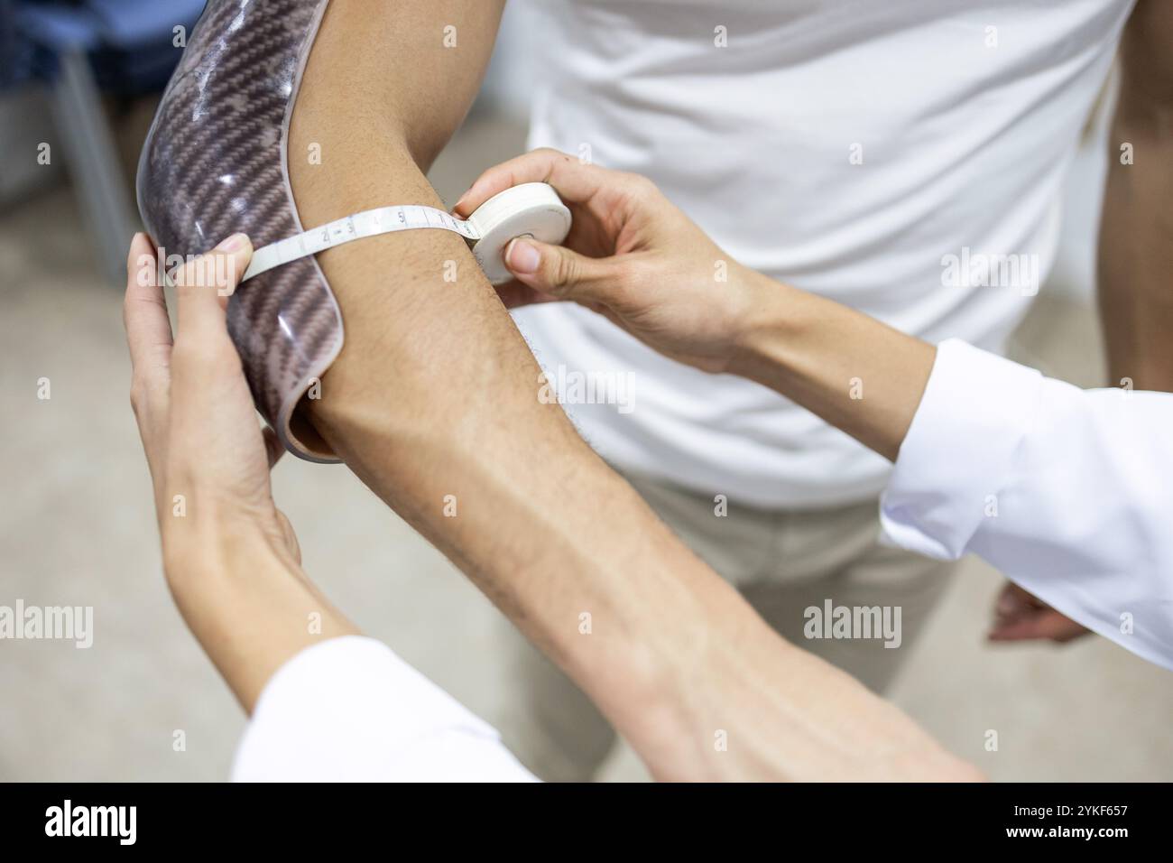Ein Fachmann misst den Arm eines Patienten, um die richtige Passform für eine individuelle orthopädische Bandage zu gewährleisten. Der Prozess unterstreicht Präzision und Sorgfalt bei Orthopedi Stockfoto
