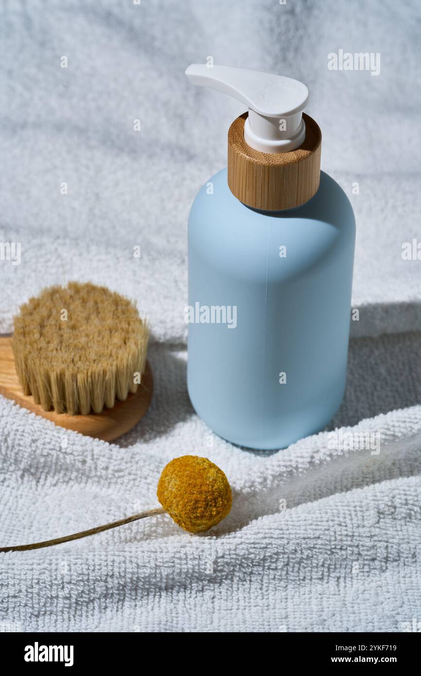 Eine stilvolle blaue SPA-Kosmetikflasche mit einer Pumpe aus Holz, begleitet von einer natürlichen Bürste und einer getrockneten Blume auf einem weißen strukturierten Handtuch, perfekt für ein Wohlbefinden Stockfoto