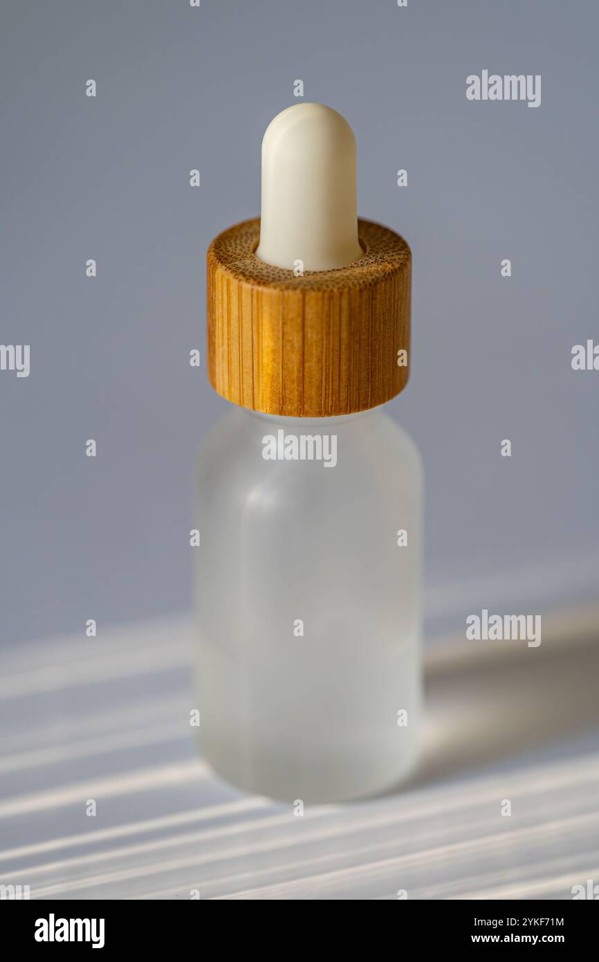 Transparente Kosmetiktropfflasche, mit Holzdeckel verschlossen und in sanften Sonnenstrahlen getaucht. Die geringe Schärfentiefe unterstreicht das schlanke, ergonomische Design Stockfoto