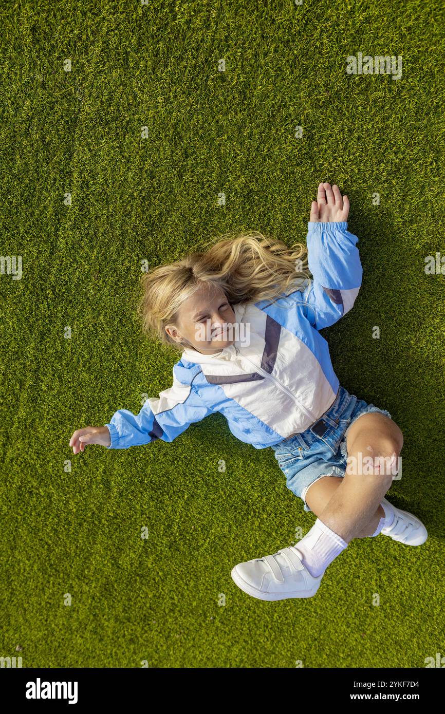 Eine junge Frau mit Stuve-Wiedemann-Syndrom, die glücklich auf üppigem, grünem Gras liegt, von oben gesehen, und trotz ihrer Konditanz einen positiven Moment in ihrem Leben zeigt Stockfoto