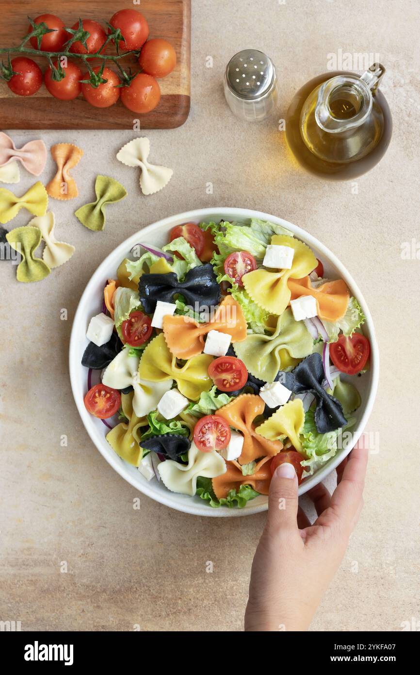 Blick von oben auf eine nicht erkennbare Person, die eine lebendige Schüssel farbiger Farfalle-Pasta mit Kurkuma, Spinat, Rote Bete, Paprika und Tintenfisch hält. Suruu Stockfoto